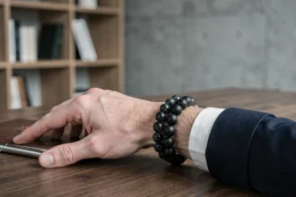 Bracelet perle homme en onyx noir porté au poignet sur un bureau en chêne foncé avec accessoires lifestyle minimalistes